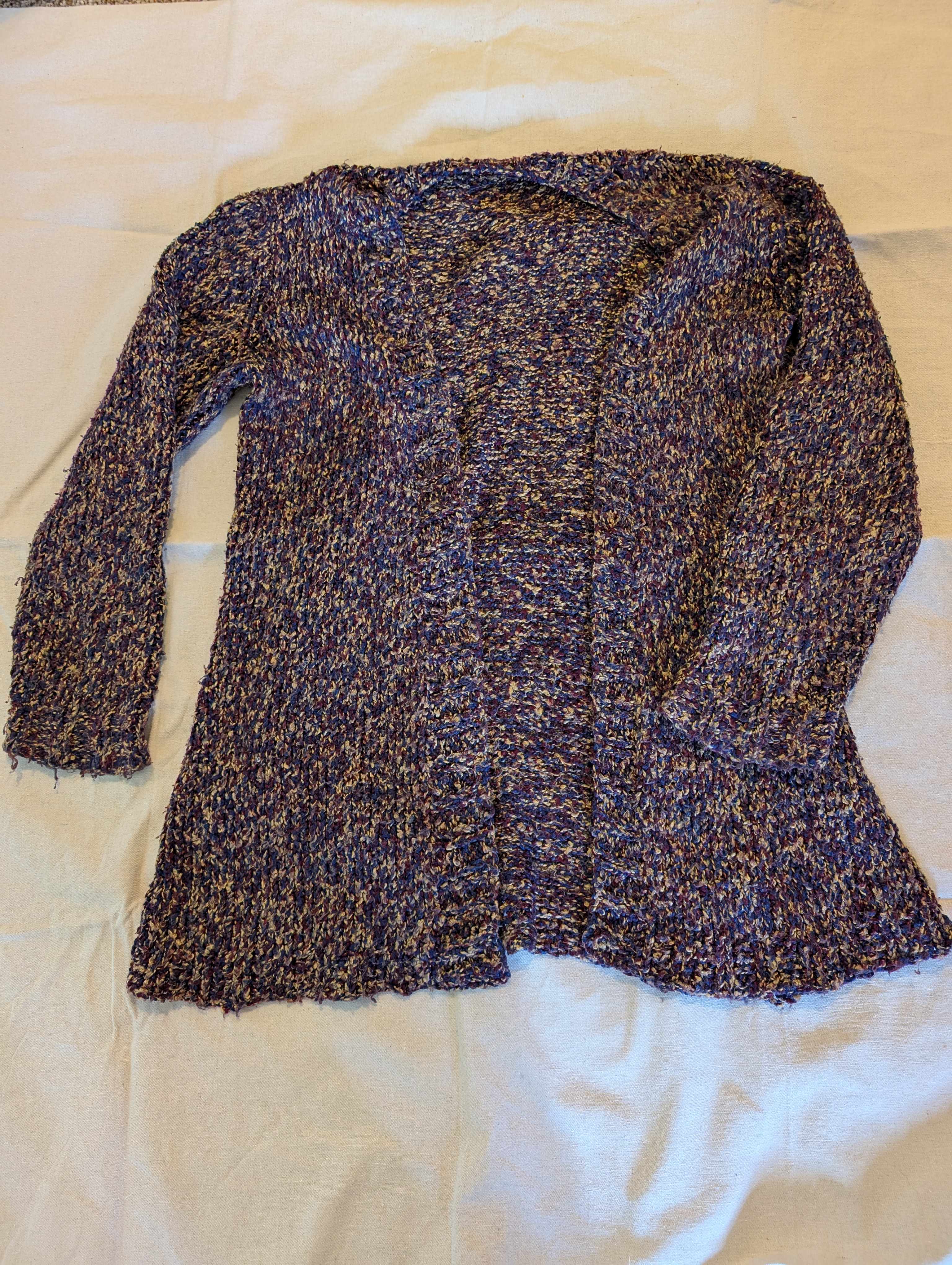 The object is a long sweater made from a simple knit stitch. It is made of multi-colour yarn in blue, red, and gold.