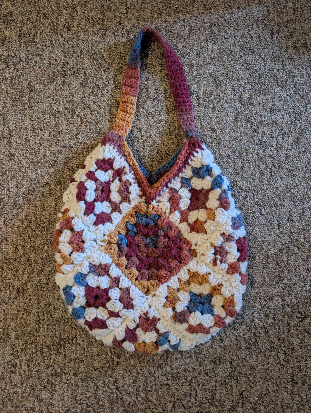 A circular bag made out of granny squares and lined with fabric. The project is made from white chunky yarn and multi-coloured blue, yellow, and red chunky yarn. The fabric inside the bag is yellow, with red dots scattered throughout. 